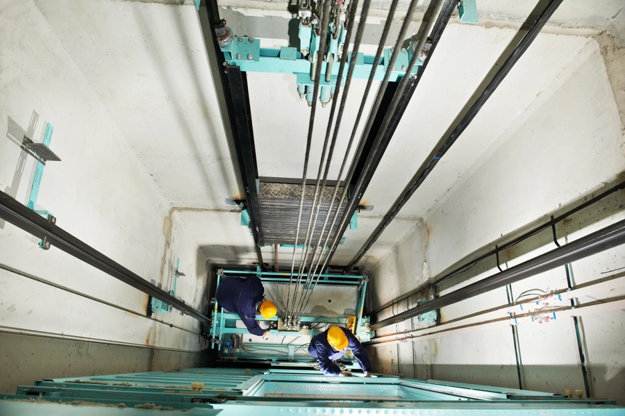 Two lift engineers working inside an elevator shaft during maintenance
